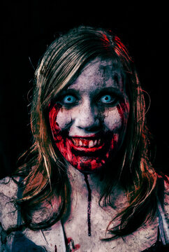 Studio portrait of a female vampire of zombie looking at camera. Black background.