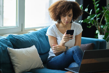Obraz premium young african-american businesswoman using laptop, while holding smartphone