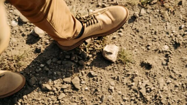 Close-up of a hiker's feet in brown boots. Walking in a hike on a steep terrain on the trail on the ground, going down from the mountain, around the grass and branches. Travelling concept. Sunny day, 