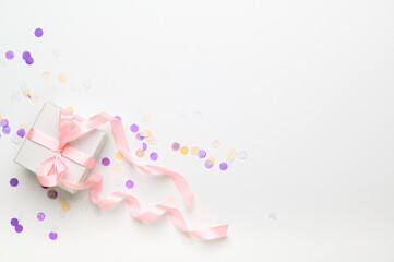 White box wrapped in pink ribbon on a white background top view. Gift for a holiday, christmas, birthday, women's day in pastel colors. Festive decor with confetti and present flat lay. Copy space