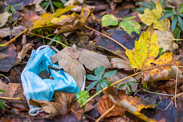 Corona mask trash in the dirt in colorful autumn leaves in Germany