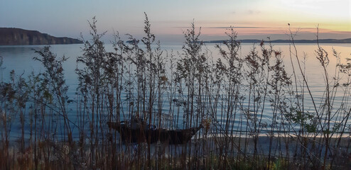 sunset over the see. a boat at the seaside. view through th high dry grass