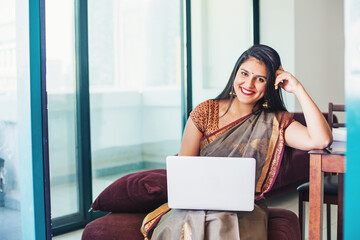 Beautiful Indian young woman in a saree using her laptop, working from home