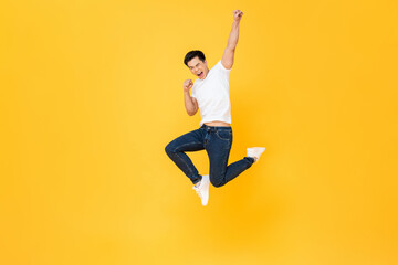 Young energetic Asian man  jumping and raising his fist isolated on yellow color background