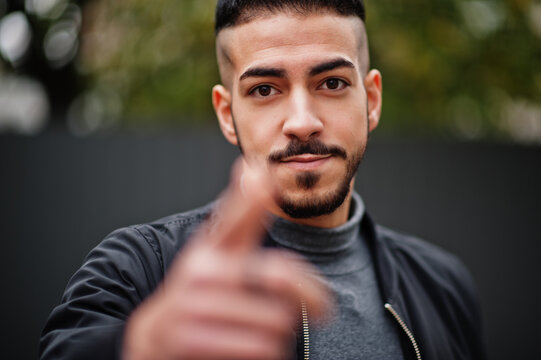 Portrait of stylish arab beard man wear grey turtleneck and black jaket. Arabian model guy show finger close to camera.