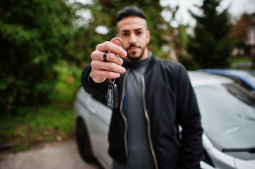 Portrait of stylish arab beard man wear grey turtleneck and black jaket. Arabian model guy stand near his car and show keys.