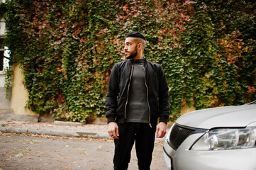 Fototapeta na wymiar Portrait of stylish arab beard man wear grey turtleneck and black jaket. Arabian model guy stand near his car.