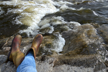 A traveler at a halt on the bank of a river. A traveler in rubber boots made a halt by the river. Camping by the river. Pause in business. Rethinking and Meditation.