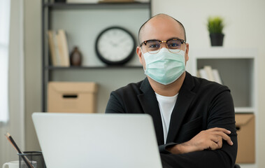 Young businessman wearing protection mask working with laptop in office. Social distancing safety from corona virus flu.