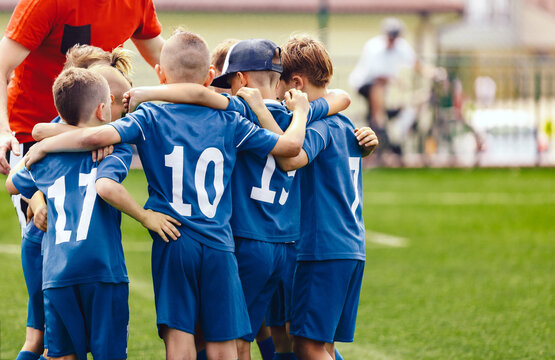 Kids in elementary school sports team with coach. Boys in blue soccer uniforms with white numbers on back. Coach motivate children football players before the game. School sports tournament for youth © matimix