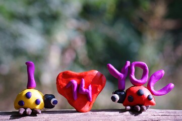 Figurines of two ladybirds made of plasticine. There's a heart between them. Next to it is the inscription I love you.