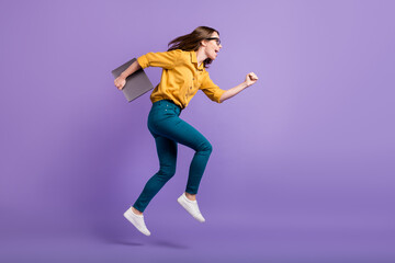 Fototapeta na wymiar Full length profile photo of lady open mouth jump hold pc wear yellow shirt blue trousers sneakers isolated violet color background