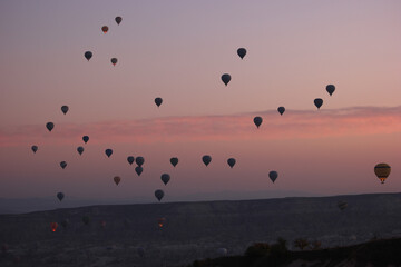 Colorful hot air balloons flying over mountains. Beautiful sunset sky on the background. Touristic place at Turkey.