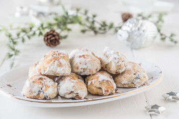 Sweet mini stollen on a christmas plate on a white wooden table, decorated with green branches and silver christmas tree decorations