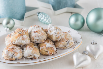 Sweet mini stollen on a christmas plate on a white wooden table, decorated with shimmering light green candles and christmas baubles and hearts