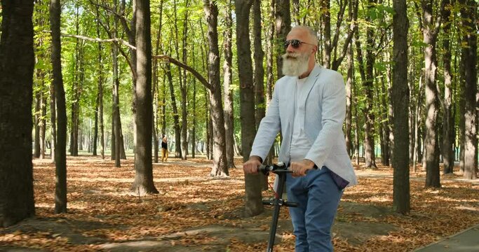 Elderly senior businessman riding electric scooter in a city park