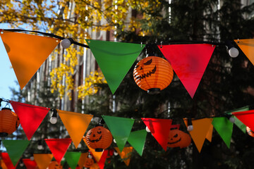 Colorful party flags and orange pumpkin lamps. Jack-o-lanterns hanging outdoors. Halloween street decoration, autumn holiday concept
