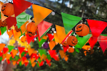 Colorful bunting paper cut, orange pumpkin lamps. Jack-o-lanterns hanging outdoors. Halloween street decoration, autumn holiday concept