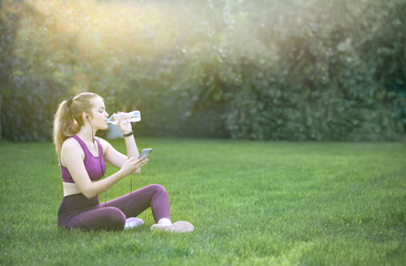 Fototapeta premium Young Smiling Blonde Athletic Girl Sitting On Grass In A Park With Smartphone And Earphones