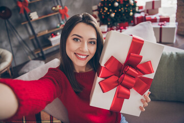 Obraz na płótnie Canvas Photo of positive girl hold gift box make selfie sit couch in house indoors with x-mas christmas decoration