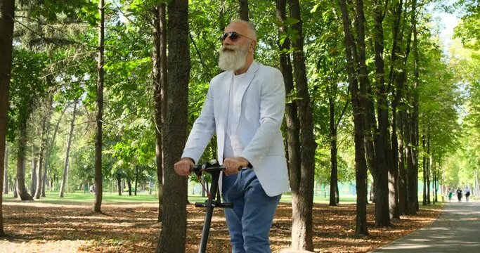 Handsome senior man riding electric scooter in a city park