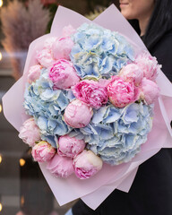 Young woman holding big beautiful blossoming bouquet of fresh peonies and hydrangea flowers in bright colors.
