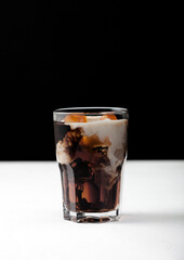 Glass of black coffee with ice cubes and fresh milk on white board and black backdrop.