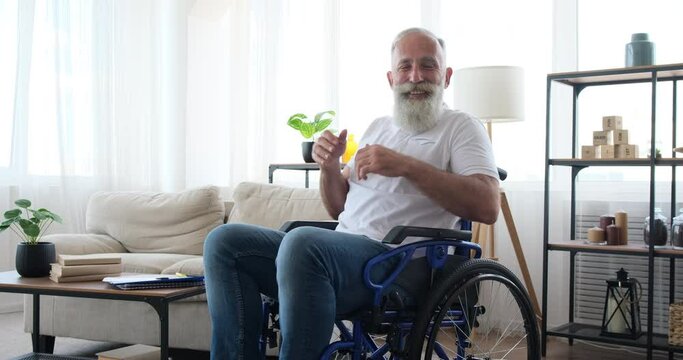 Smiling disabled senior man sitting on wheelchair at home
