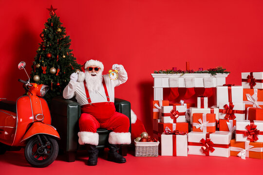 Nice attractive fat overweight cheerful Santa father sitting in armchair showing time fast delivery holly jolly festal day isolated over bright vivid shine vibrant red color background