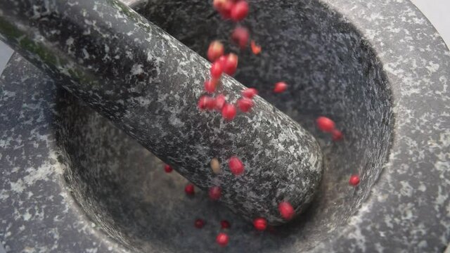 Close-up of spicy rose peppercorns falling into the grey stone mortar in slow motion