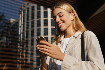 Obraz na płótnie Canvas Nice happy blonde girl using mobile phone while walking at street
