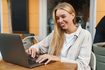 Nice happy blonde girl working with laptop while sitting in cafe
