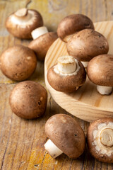 Top view of raw portobello mushrooms, on wooden board and rustic table, with selective focus, vertical