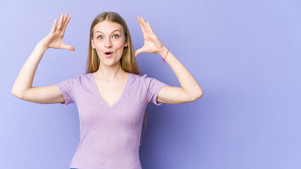 Fototapeta na wymiar Young blonde woman isolated on purple background celebrating a victory or success, he is surprised and shocked.