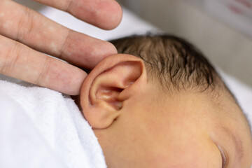 Fototapeta na wymiar Hand Lifting New Born Baby Girl's Ear