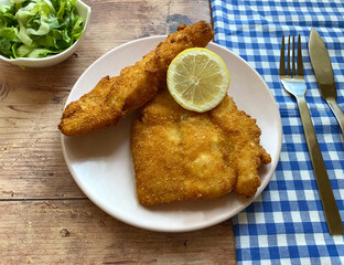 Breaded cod fish fillet, also known as Kabeljau. The fish is coated in egg, flour and breadcrumbs, then deep fried to golden brown and served with green salad with Vinaigrette and lemon.