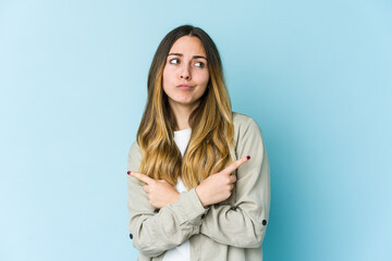 Obraz premium Young caucasian woman isolated on blue background points sideways, is trying to choose between two options.