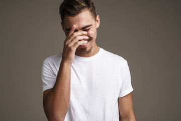 Image of joyful unshaven guy laughing and covering his face