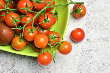 Close up, Cherrys tomatoes on branch on green plate, light stone background, space for text