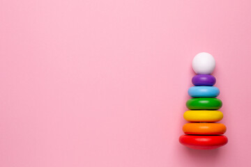 Colorful children's wooden pyramid on a pink background, toy for toddlers and babies with copyspace