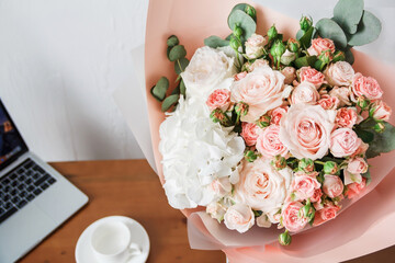 Lovely bouquet with pink roses close-up. Background for congratulations and place for text. Flowers for birthday. A bouquet of flowers stands on the table, next to a blurred laptop and a white cup.