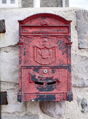 Red metal mailbox with peeling paint on a stone wall