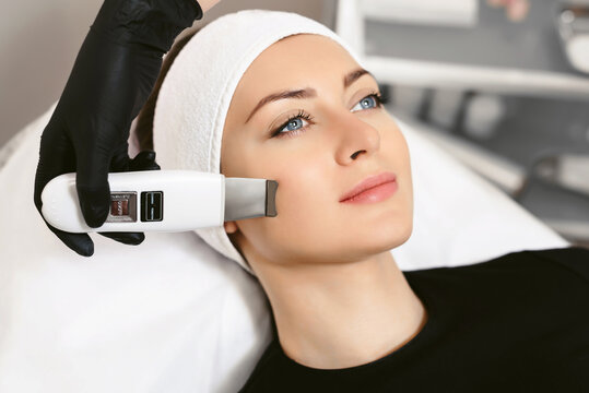 Beautician with Ultrasonic scrubber. Doctor doing procedure of ultrasonic cleaning of face. Cosmetological clinic. Patient. Healthcare, clinic, cosmetology