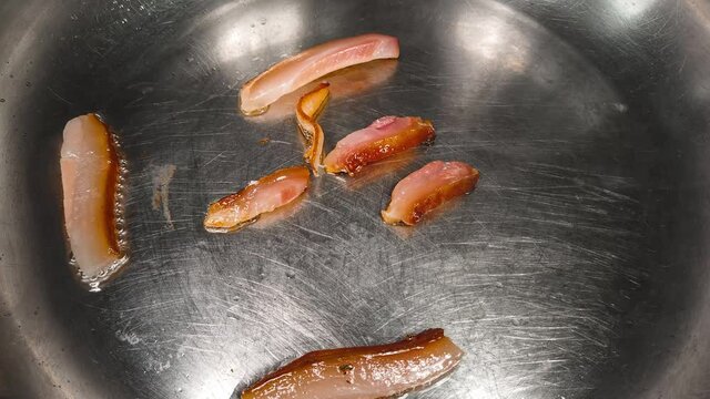 Timelapse of slices of bacon fat slowly rendering and sizzling in stainless steel pan