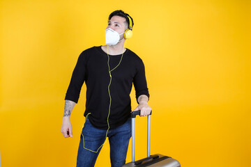 man with protective mask suitcase and passport, listening to music, his flight is delayed by...