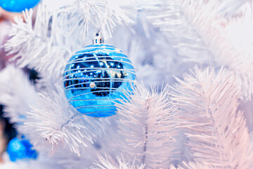 Blue Christmas balls hangs on white artificial fir tree
