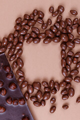 Chocolate bar with nuts and chocolate balls on the beige background with empty square space for text in center . Peanuts in chocolate glaze. Chocolate bar with hazelnuts. 