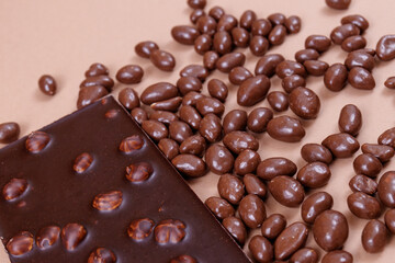 Chocolate bar with nuts and chocolate balls on the beige background. Peanuts in chocolate glaze. Chocolate bar with hazelnuts.