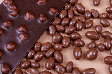 Chocolate bar with nuts and chocolate balls on the beige background. Peanuts in chocolate glaze. Chocolate bar with hazelnut.