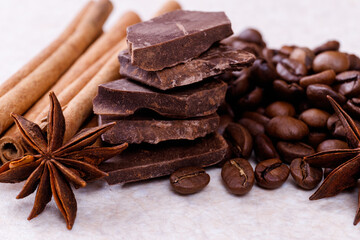 Stack of chocolate bar pieces with heap of roasted coffee beans and spices, cinnamon sticks and...